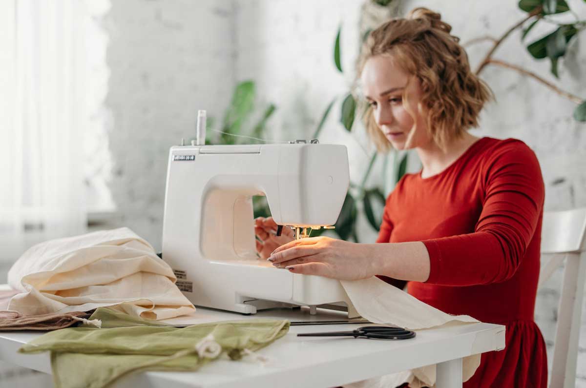Femme en robe rouge et sa machine à coudre pour une séance couture Kitac